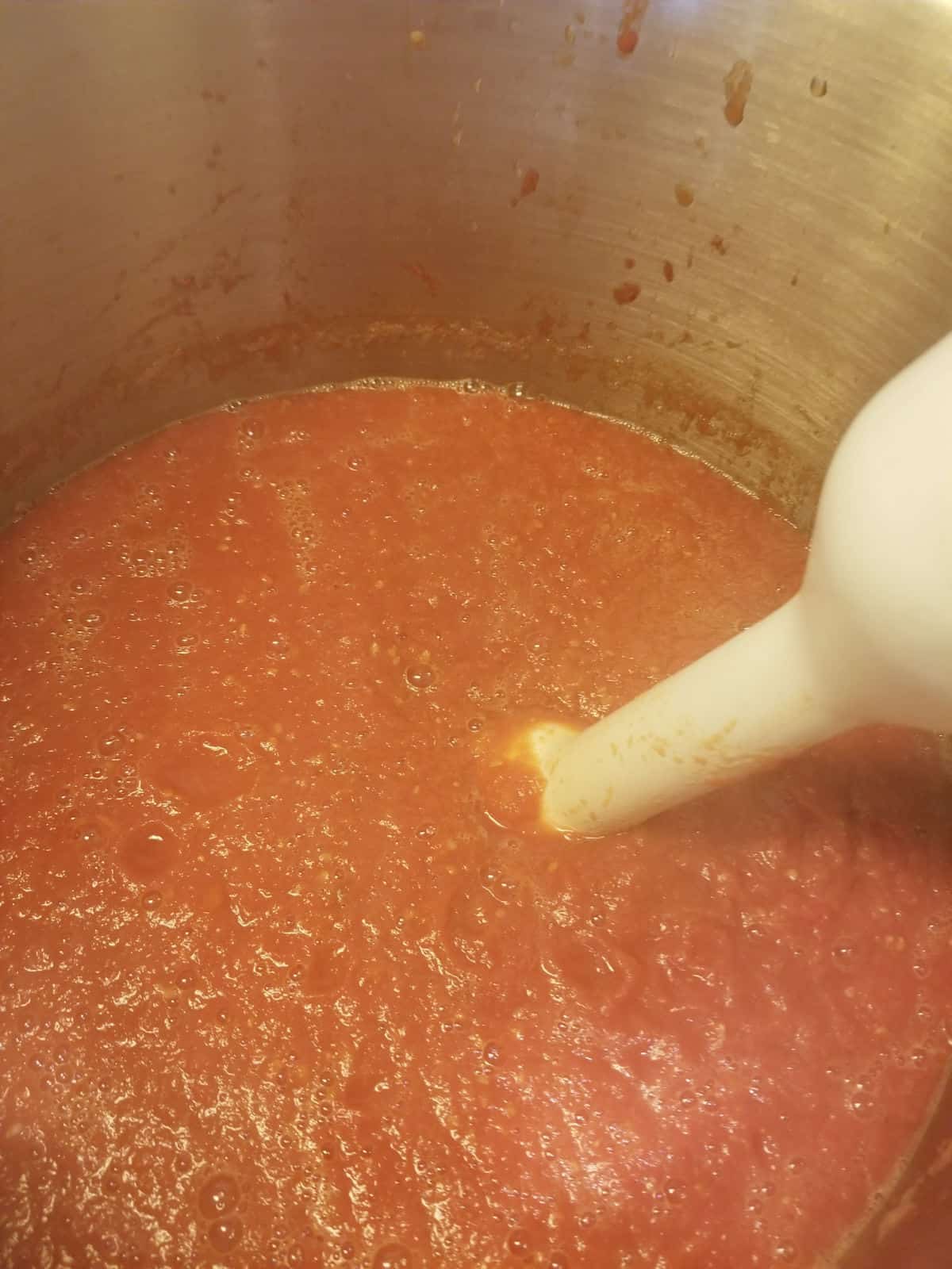 close up of an immersion blender blending a large pot of tomato sauce