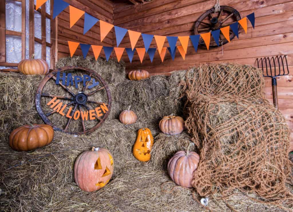 piles of hay bales with pumpkins and orange and black banner hanging above