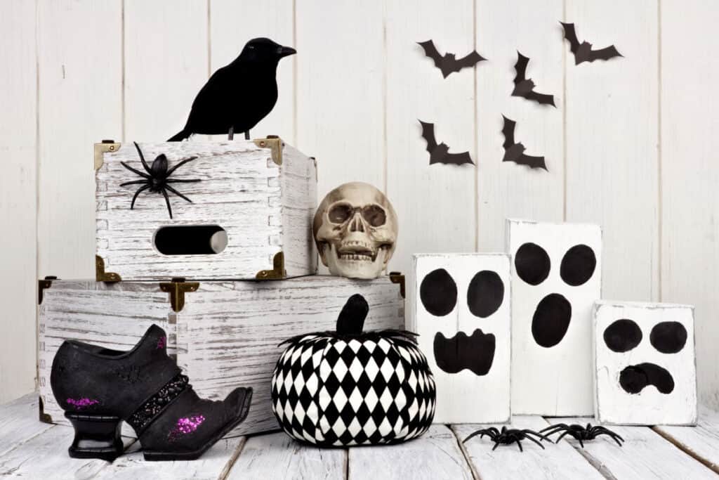 a white and black halloween display with rustic white wood boxes, spider, crows, bats, ghosts, witches shoe and harlequin pumpkin