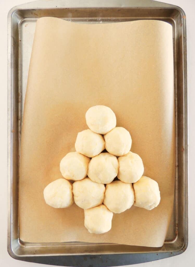 a baking sheet showing one small complete christmas tree shape with row 3 having 2 dough balls and a single ball at the top with room for another small tree on the sheet