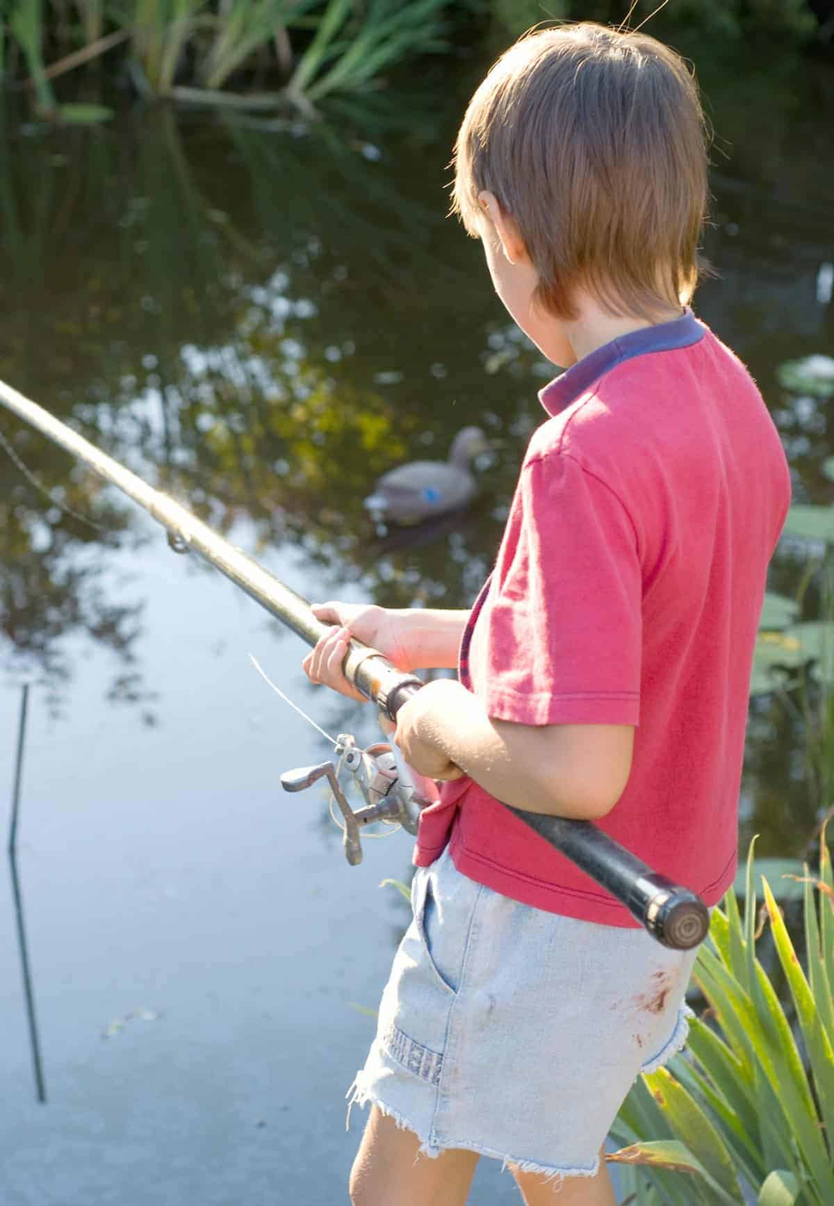 the backside of a boy fishing in a lake