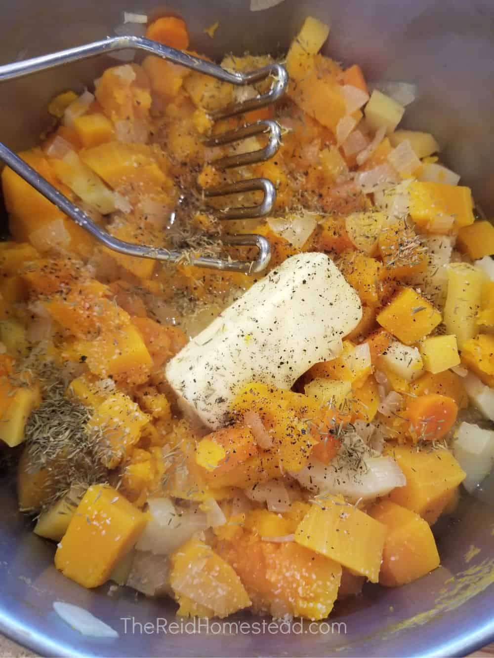 a pot full of chopped and boiled root vegetables and butternut squash with a stick of butter and a potato masher ready to be mashed