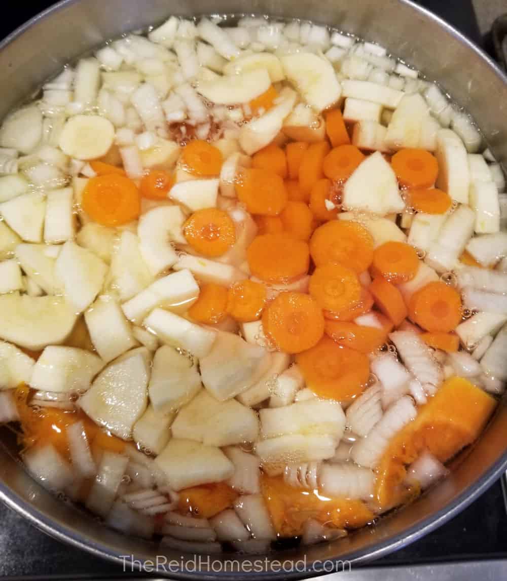 a large pot full of chopped root vegetables and butternut squash, covered in water