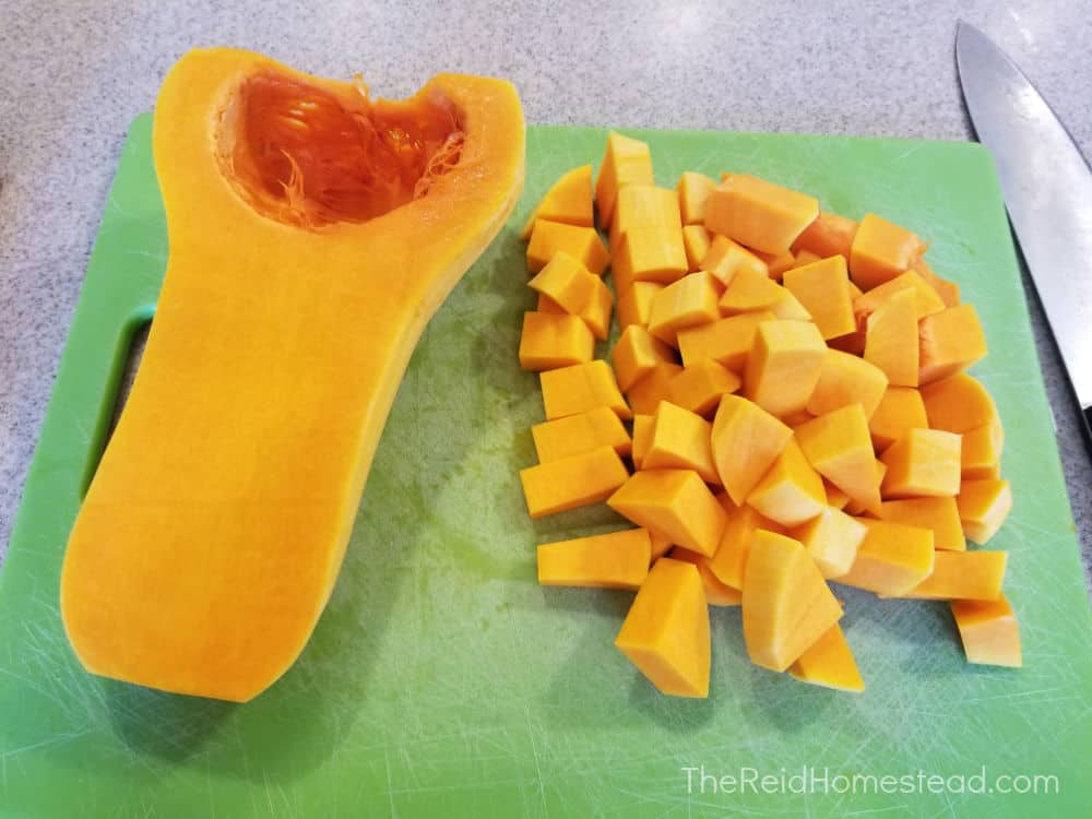 cutting board with one half of a butternut squash and the other half of squash chopped into cubes