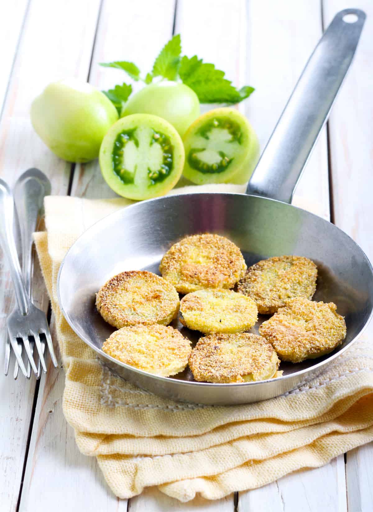 a frying pan full of fried green tomatoes with sliced green tomatoes beyond