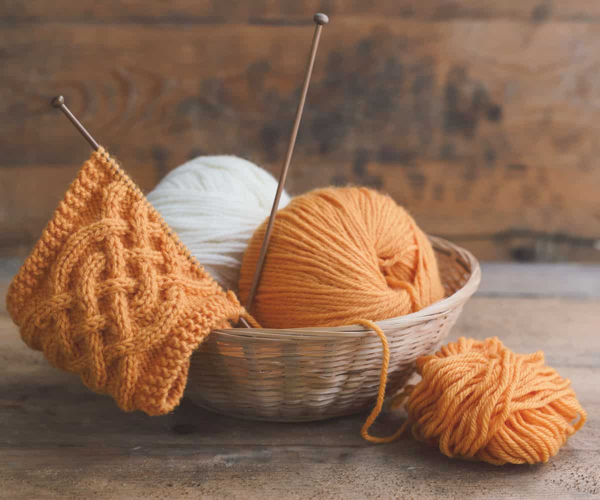 a basket with orange yarn and knitting needles in a knitting project