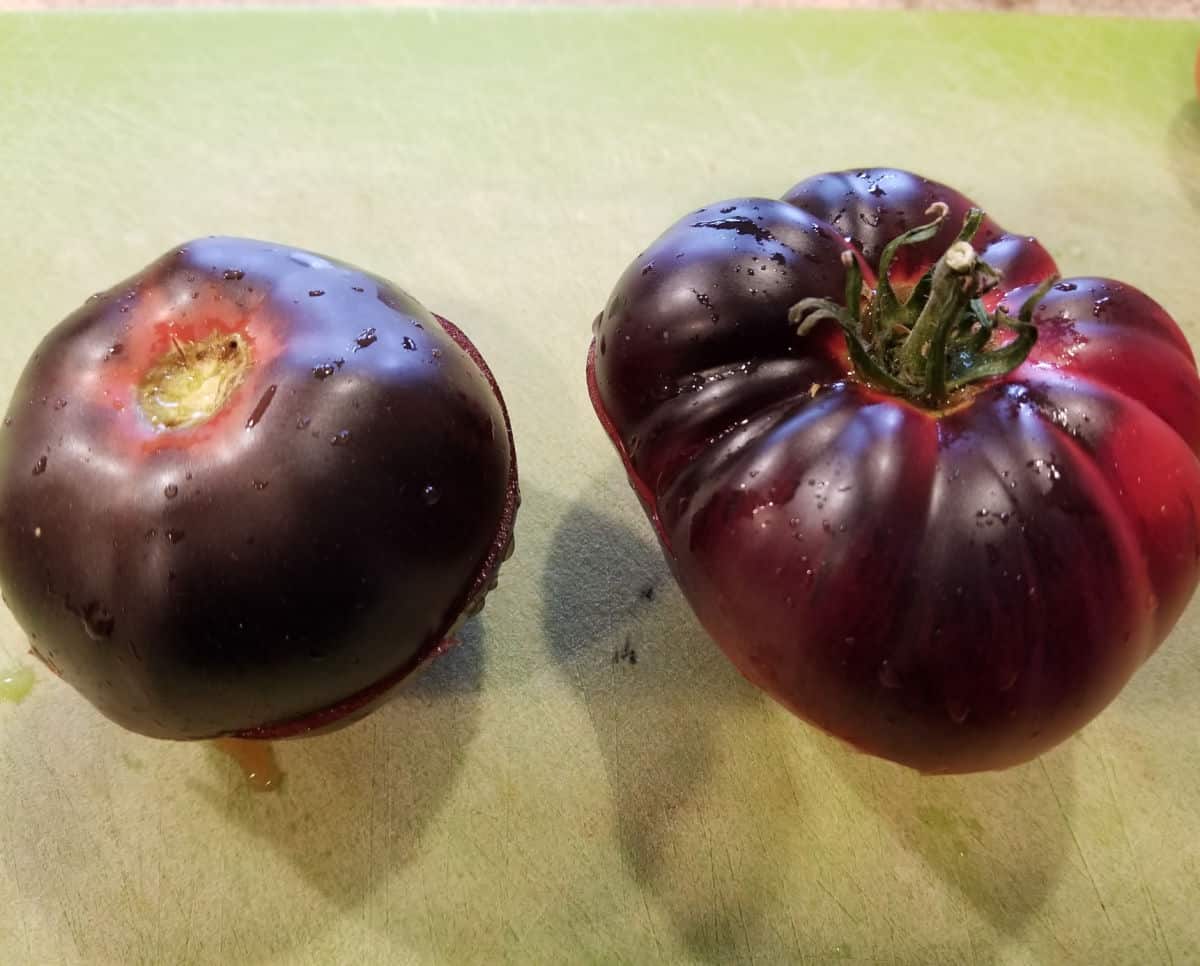a ripe black beauty and blue beauty tomato sitting side by side on a cutting board.