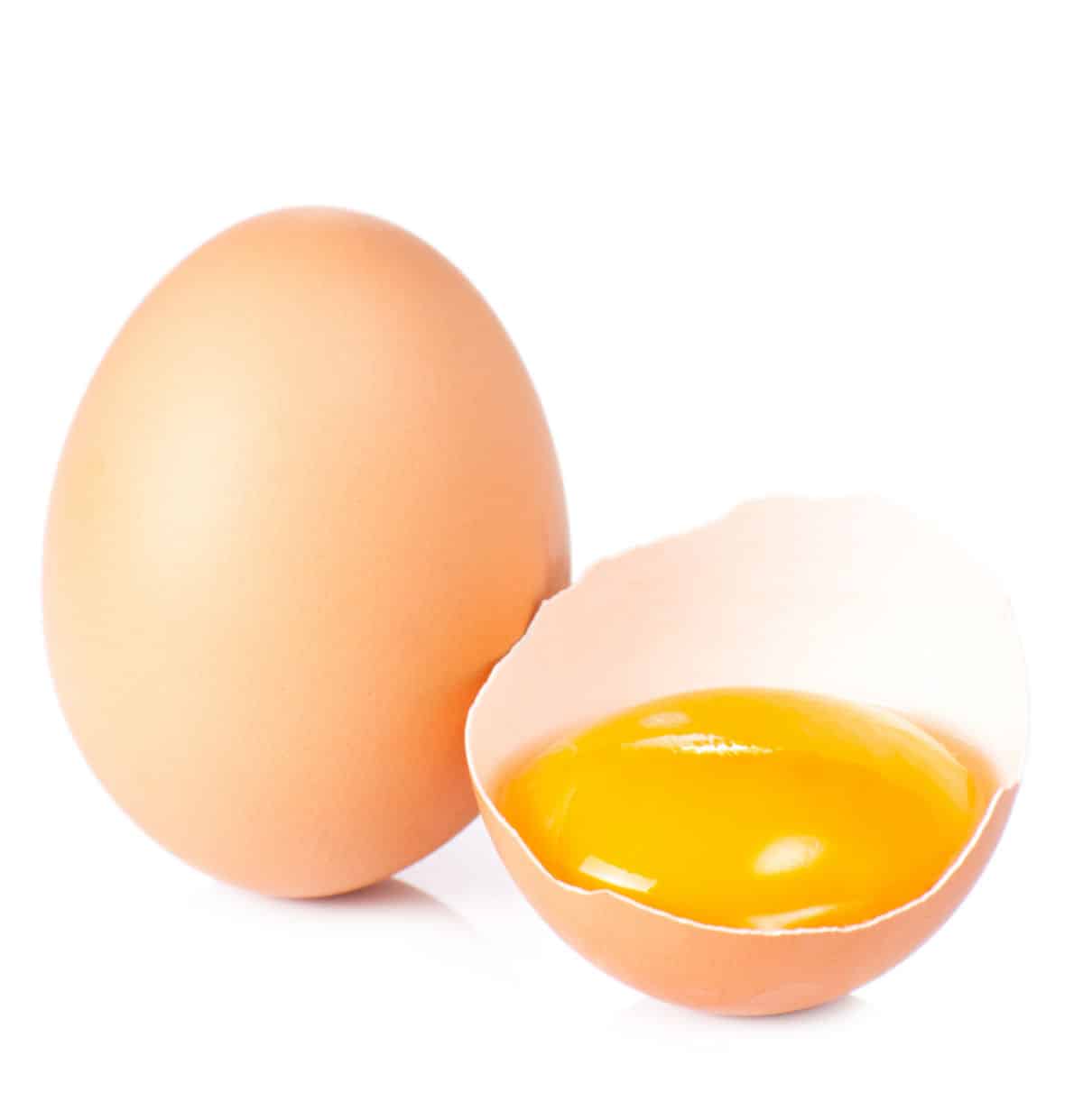 a whole brown egg with a half an egg shell with a yolk in it 