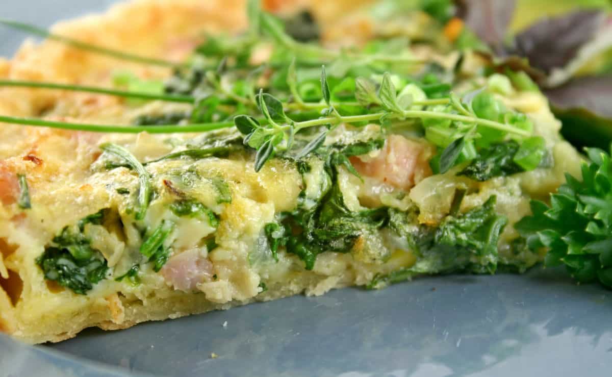 a close up of a piece of quiche with fresh herbs