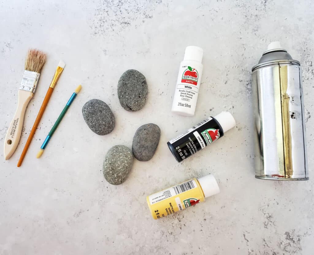 supplies needed to paint bumble bee rocks: paint brushes, rocks, craft paint and a can of clear acrylic coating spray