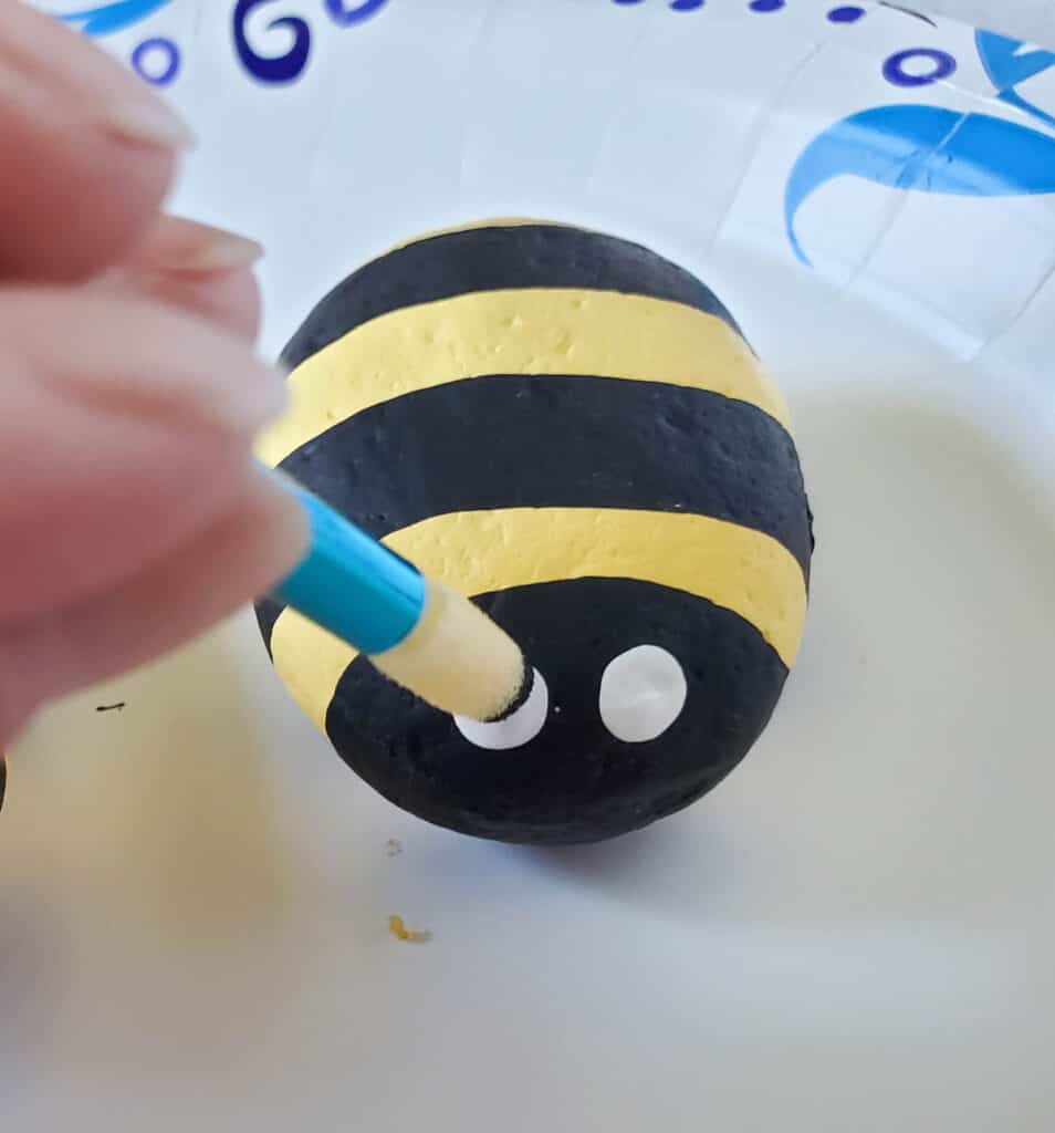 painting the black dots on the eyes on a painted bumble bee rock