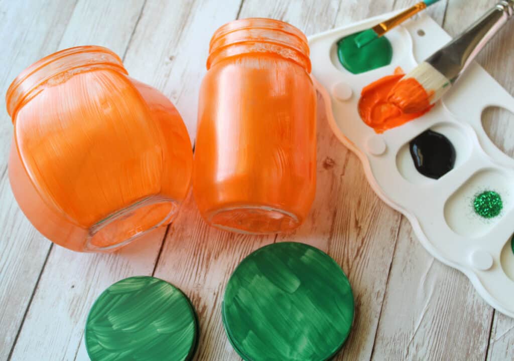 2 jars painted orange with lids painted green next to a pallet of paint