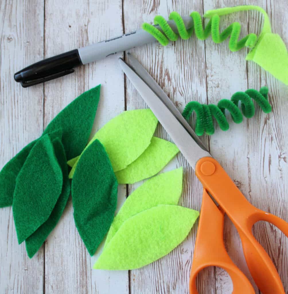 a pile of cut out felt leaves and pipe cleaner curly cures next to a permanent maker and pair of scissors