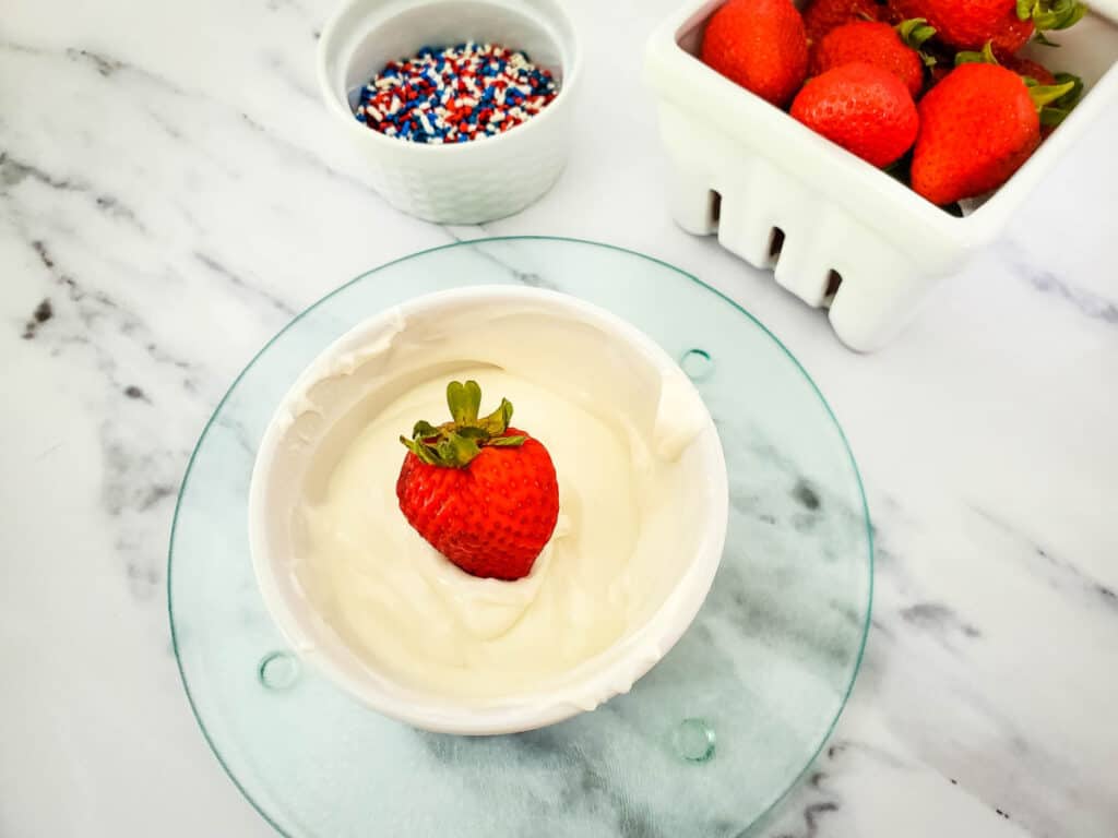 dipping a strawberry into a bowl of melted white chocolate
