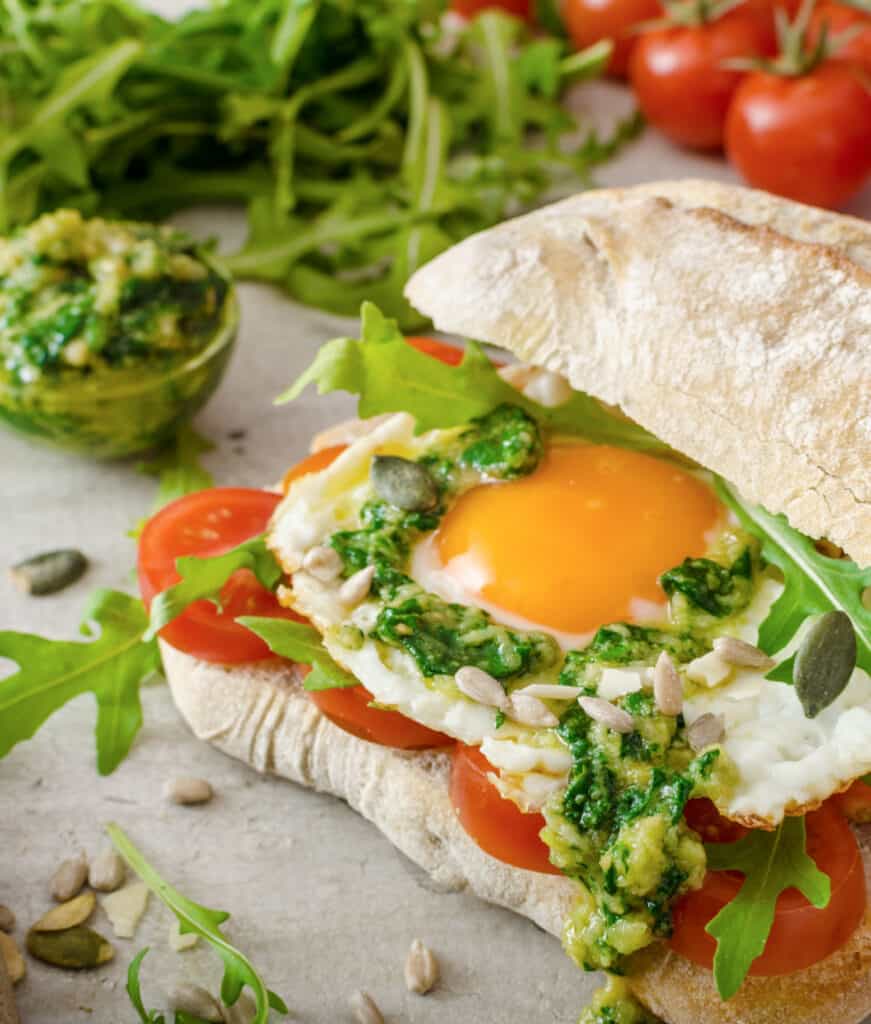 an egg sandwhich on a crusty roll with pesto and tomatoes
