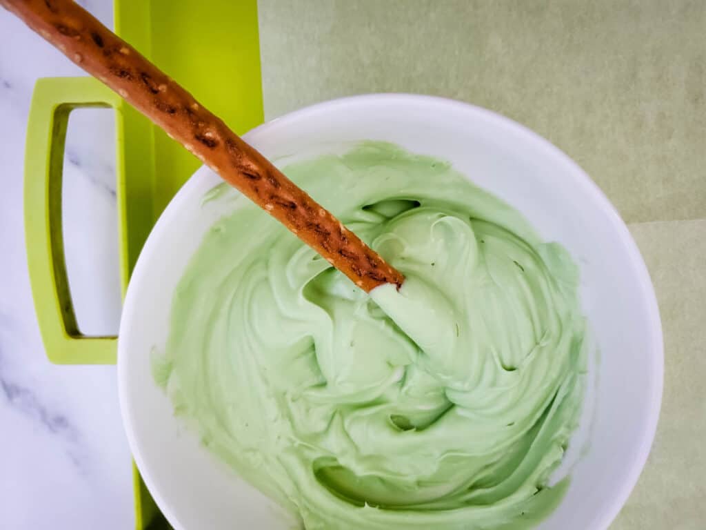 dipping a pretzel rod into a bowl of green melted candy wafers