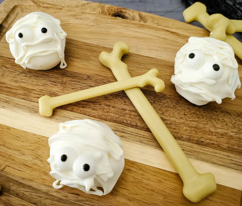 close up of 3 halloween mummy oreo cookie balls on a wood cutting board with plastic bones