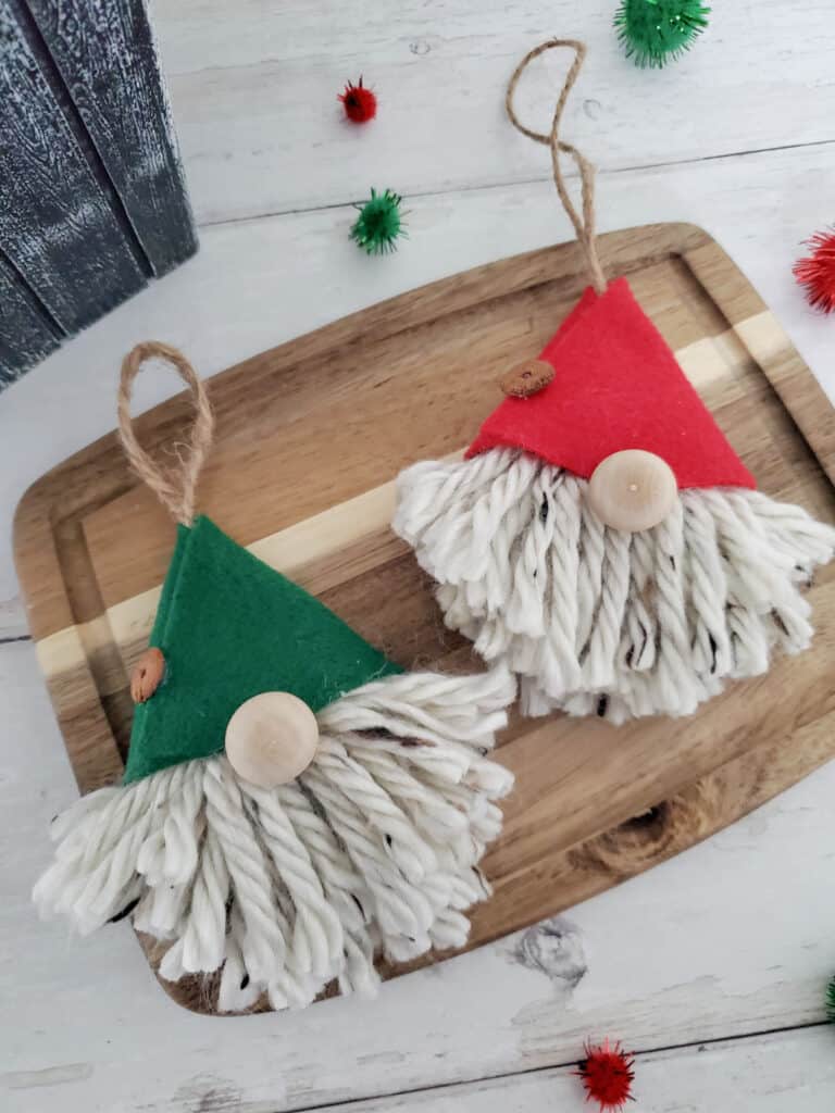 two finished gnome yarn ornaments on a wood cutting board