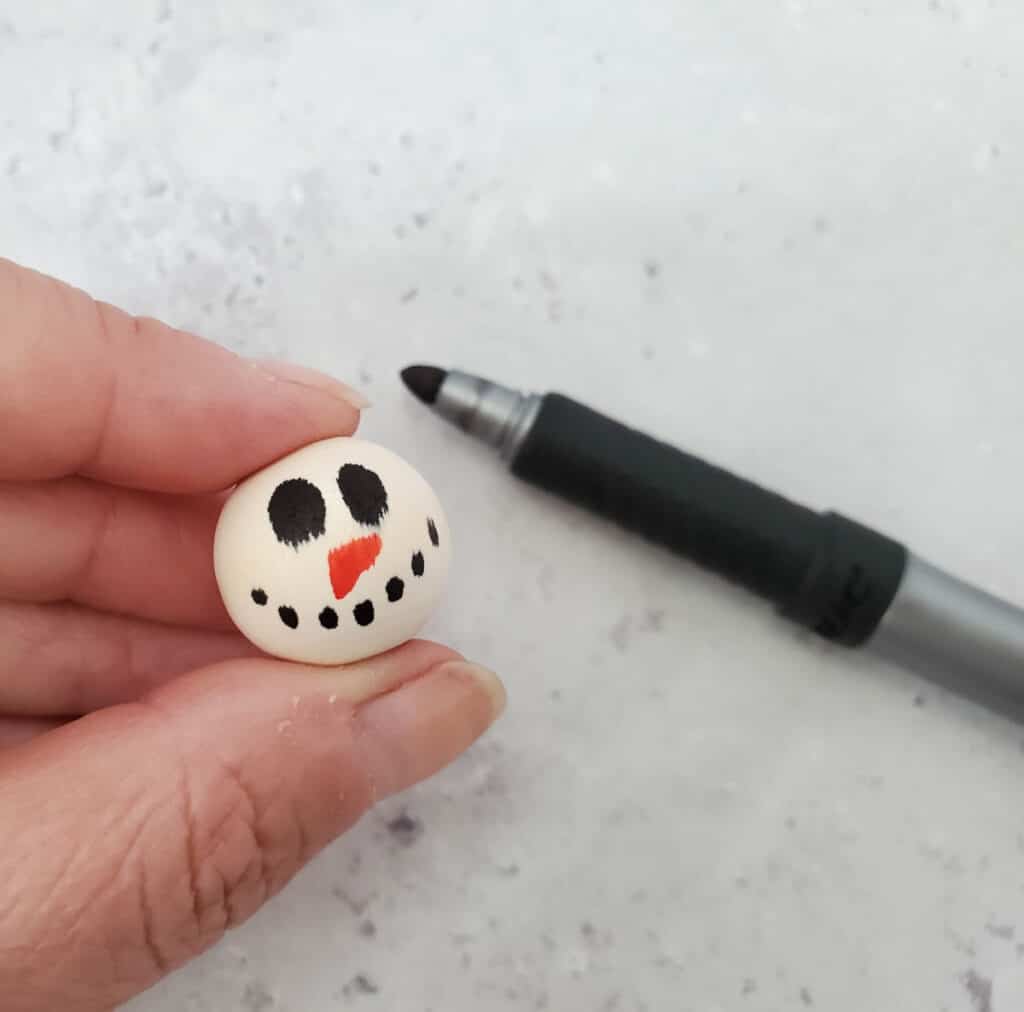 close up of drawing a dotted charcoal mouth on the snowman bead head