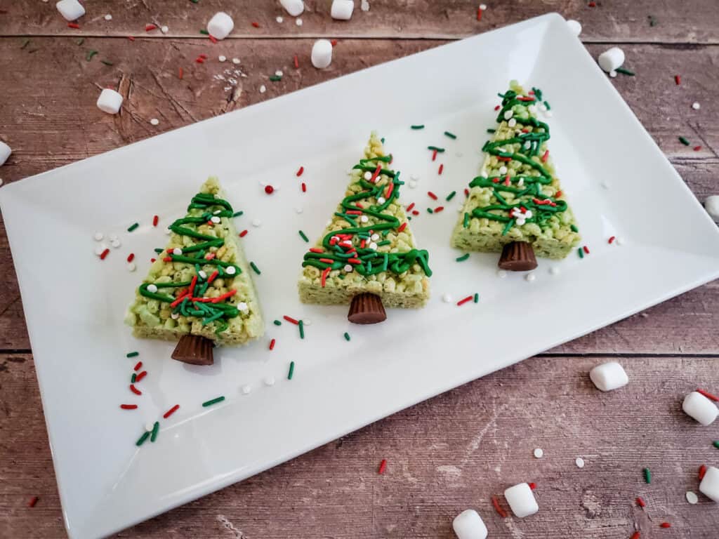close up of three finished christmas tree rice krispie treats on a white rectangular platter