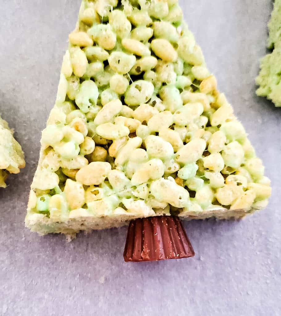 the mini reese's peanut butter cup placed onto the triangle shape of the rice krispie treat as the tree trunk