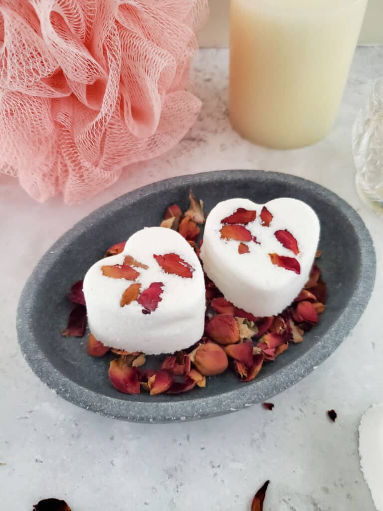two rose petal heart shaped bath bombs in a gray dish with rose petals