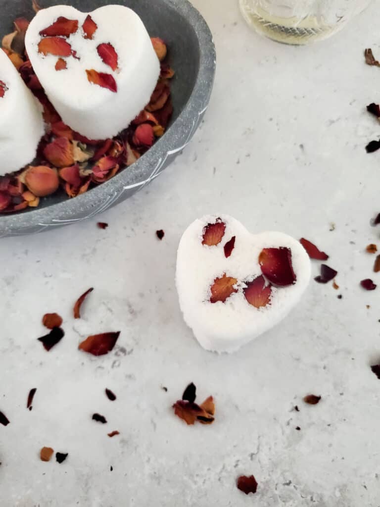 a couple of finished rose petal bath bombs with rose petals sprinkled around them
