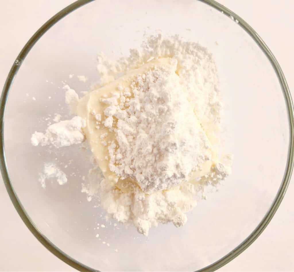 adding the cream cheese and powdered sugar to a mixing bowl
