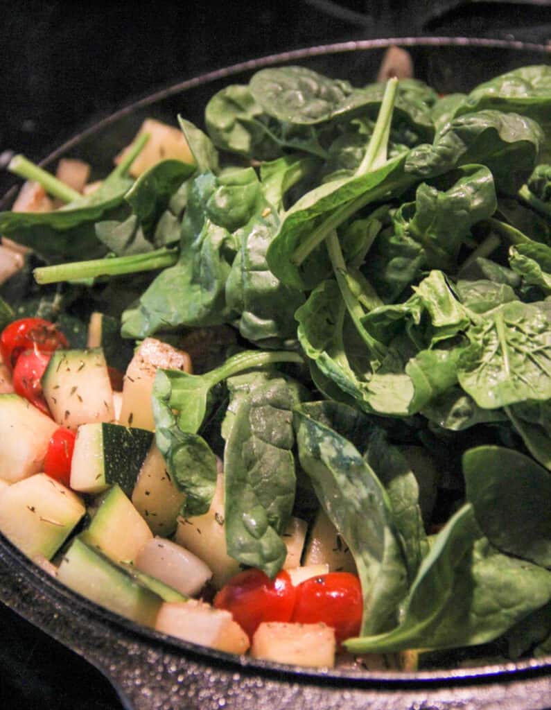 close up of the skillet with the fresh spinach leaves added 