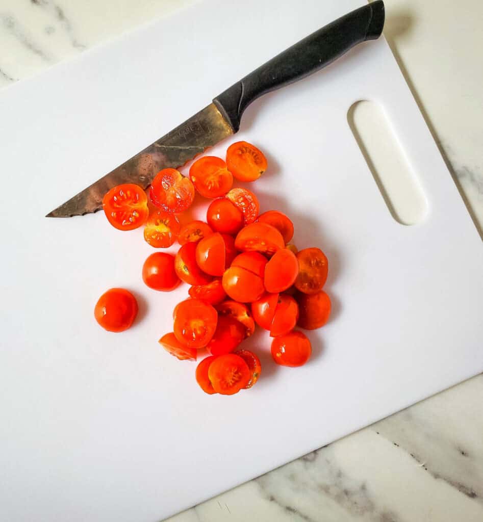 cherry tomatoes that have been cut in half on a cutting board