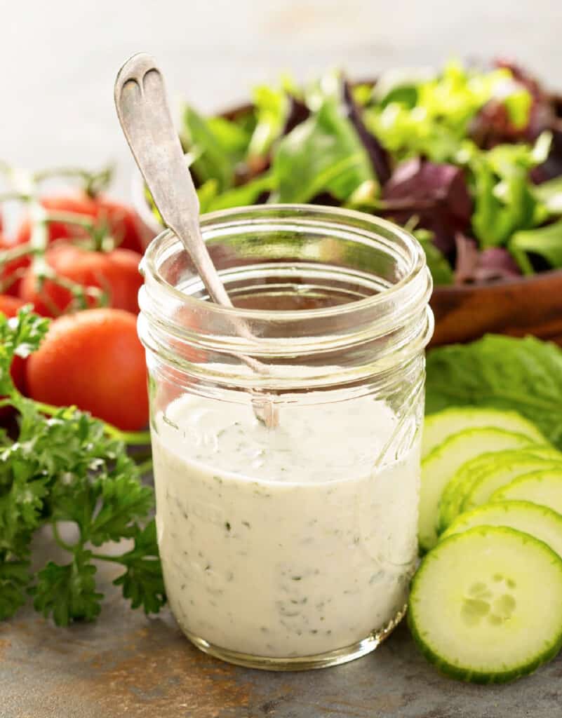 close up of a small mason jar with home made creamy ranch dressing surrounded by fresh vegetables