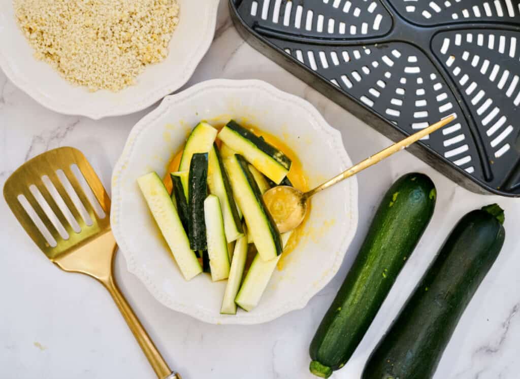 zucchini fry slices dipped in egg in a white bowl