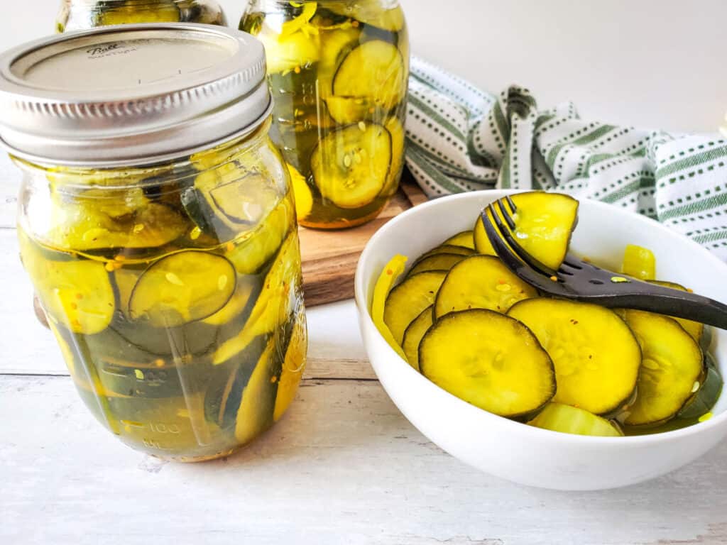 a bowl full of no cook refrigerator pickles with a fork next to a jar of pickles