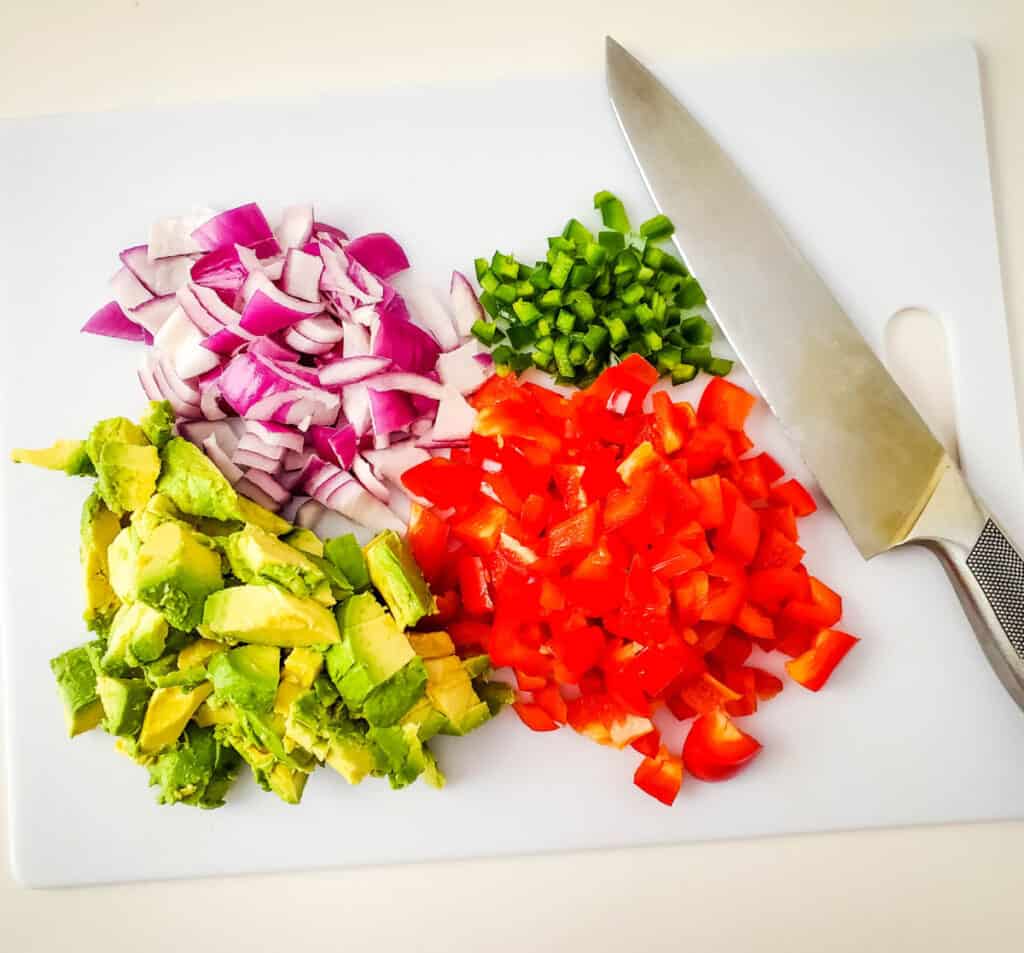 a cutting board with chopped red onions, chopped avocado, red bell pepper and jalapeno