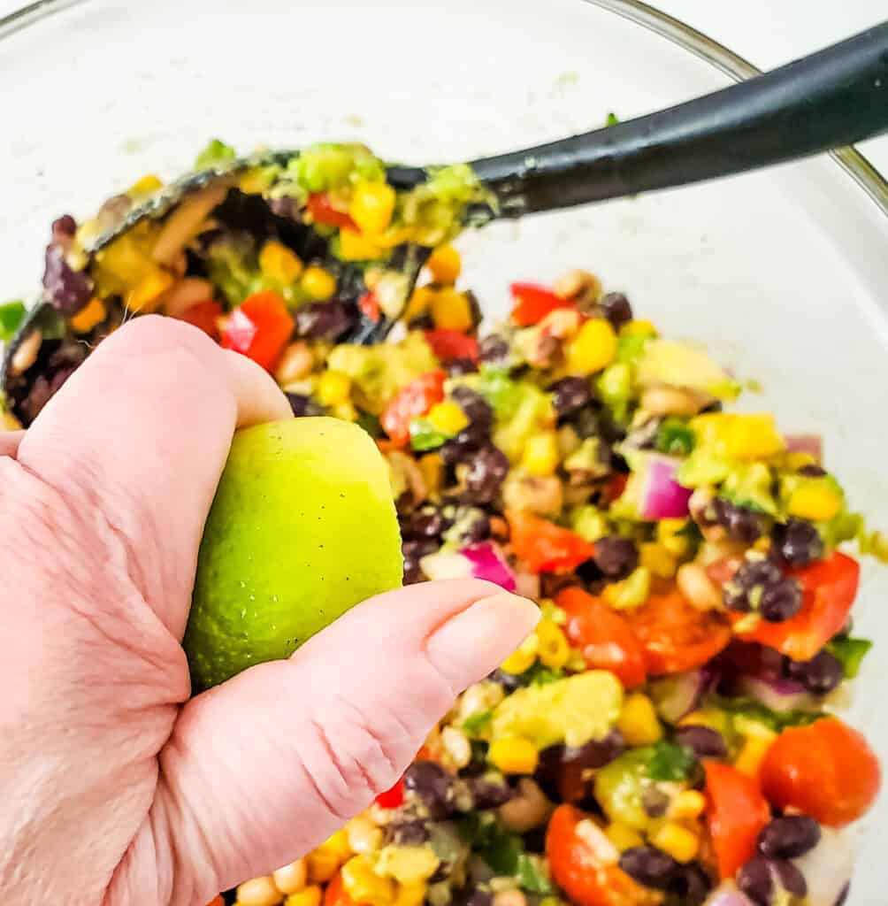 a hand squeezing lime juice into the bowl full of all the ingredients for texas caviar