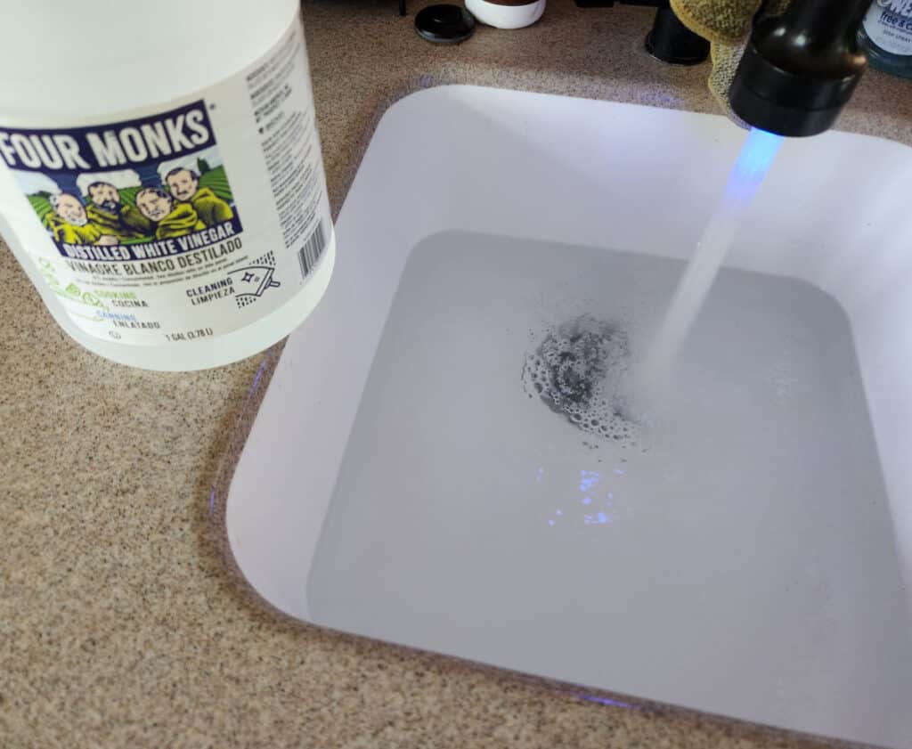 close up of a clean sink filling with water with a vinegar bottle next to it